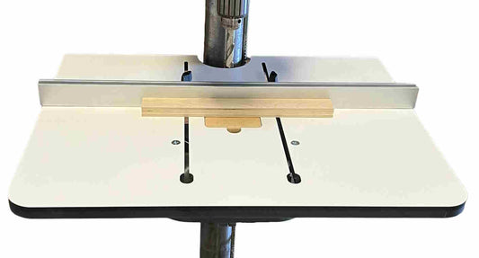 The image shows a silver-colored Woodhaven 1827 Fence attached to a drill press table, designed to guide the movement of a workpiece in drilling applications.
