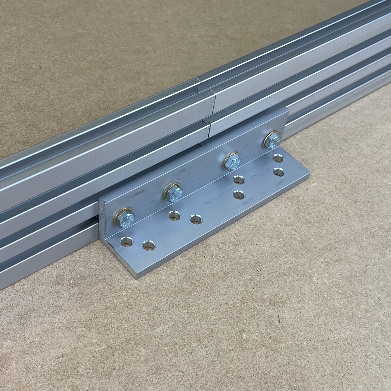 A metal track connector kit from Woodhaven, consisting of a flat metal bracket and bolts, placed on a flat surface with two tracks aligned parallel to each other.